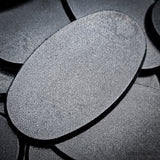 Matte black 75x42mm oval plain plastic wargaming bases with a fine textured top, injection-moulded ABS, shown in a pile.