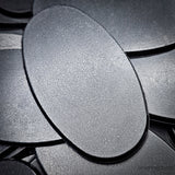 Matte black 90x52mm oval plain plastic wargaming bases with a fine textured top, injection-moulded ABS, shown in a pile.