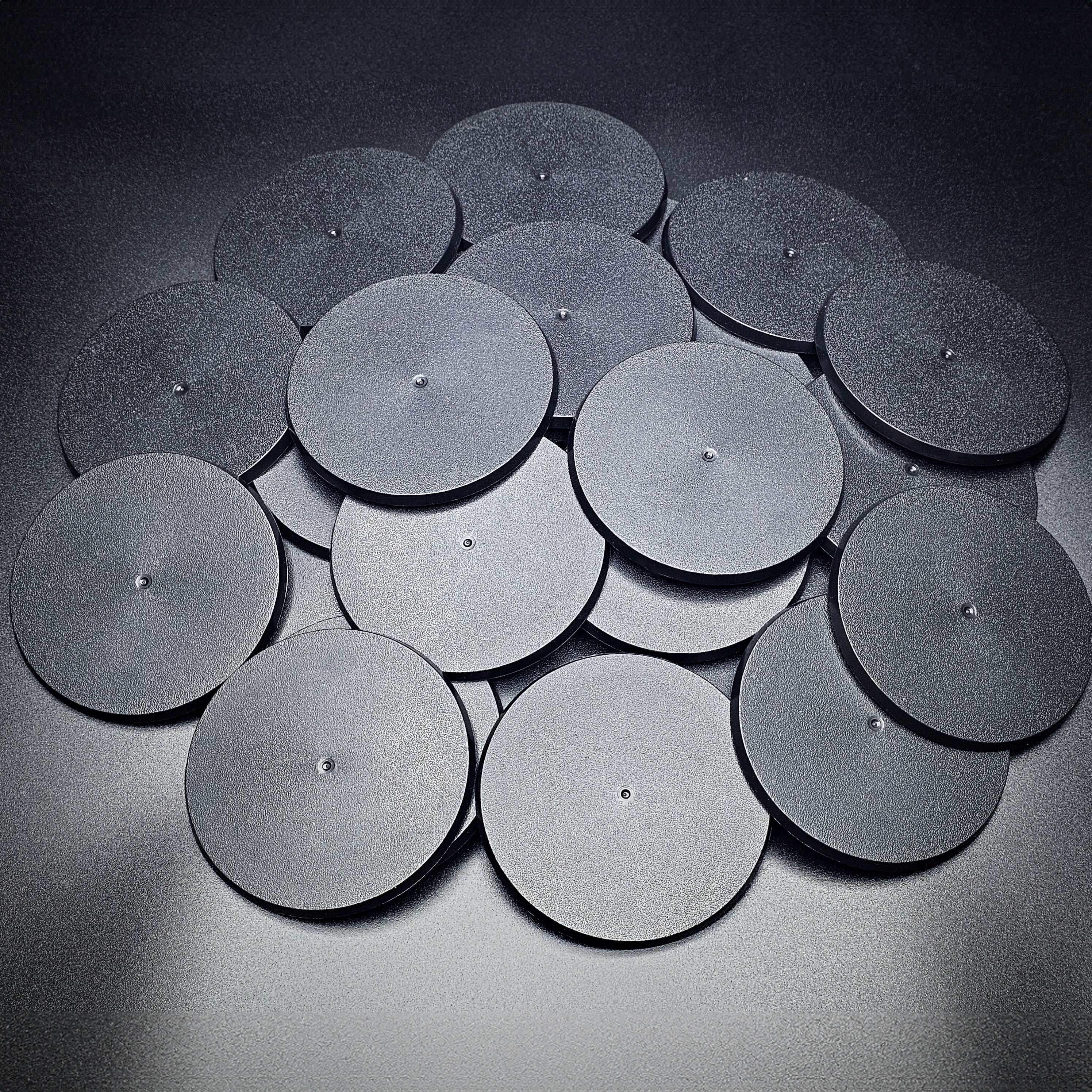 A group of 90mm round bases in a pile on a black background.