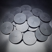 A group of 90mm round bases in a pile on a black background.
