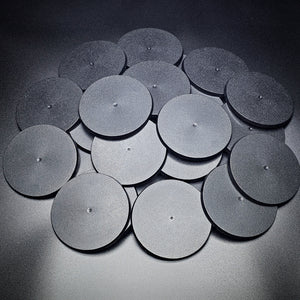 A group of 90mm round bases in a pile on a black background.