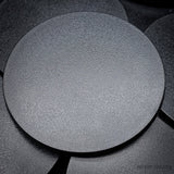 Black 100mm round plain plastic wargaming bases with a fine textured top, injection-moulded ABS, shown in a pile.