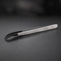 DSPIAE AT-TZ08 anti-static tweezers on dark slate, the black carbon fibre tips curving down to a hooked point