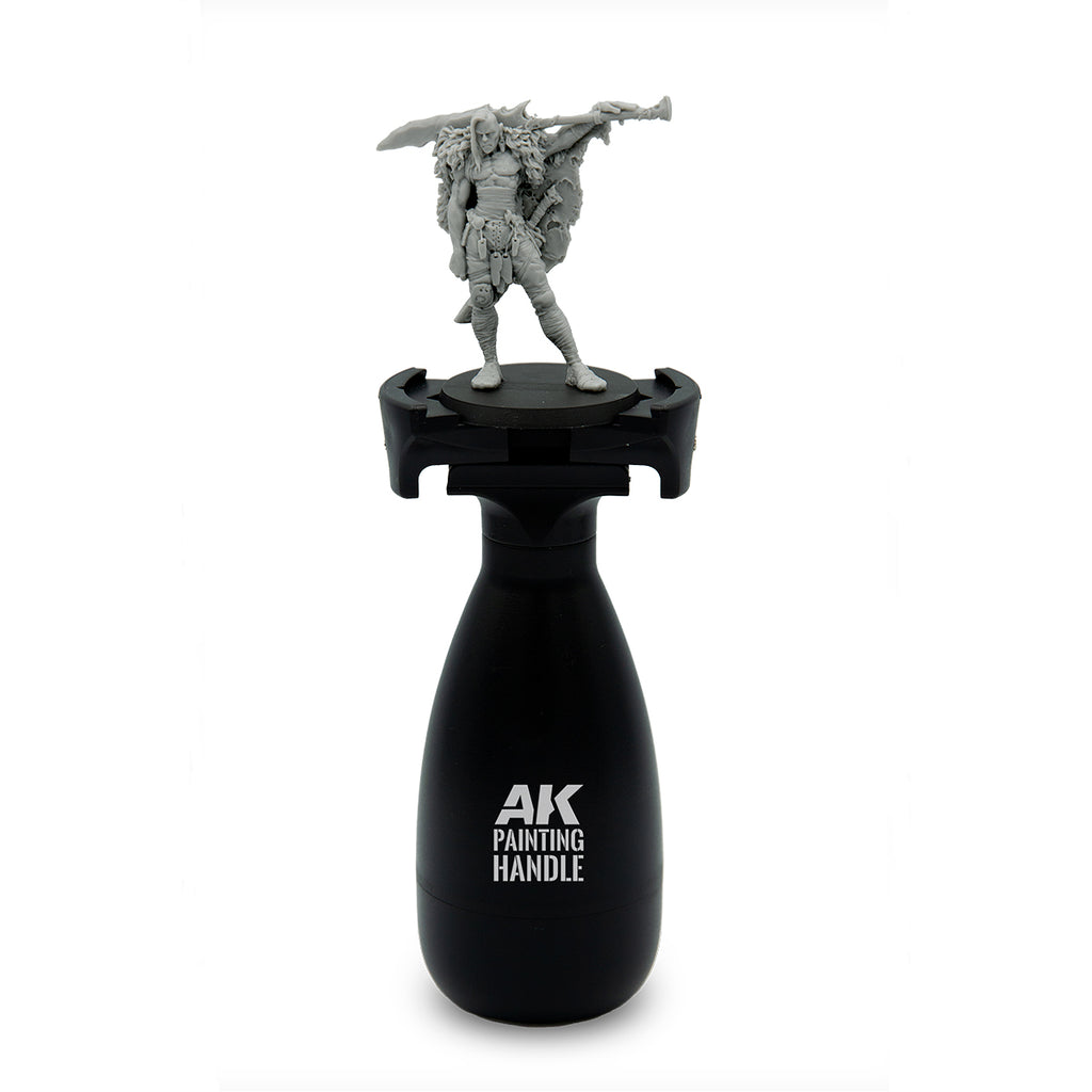 AK Interactive Painting Handle front view with unpainted fantasy warrior miniature mounted on top showing ergonomic black bottle-shaped grip body with AK Painting Handle branding