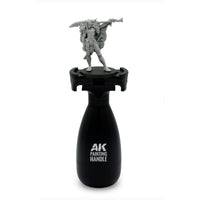 AK Interactive Painting Handle front view with unpainted fantasy warrior miniature mounted on top showing ergonomic black bottle-shaped grip body with AK Painting Handle branding
