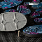 Underside of a 75mm oval base in bare grey: two magnet recesses on the centre rib, a stack of disc magnets beside it