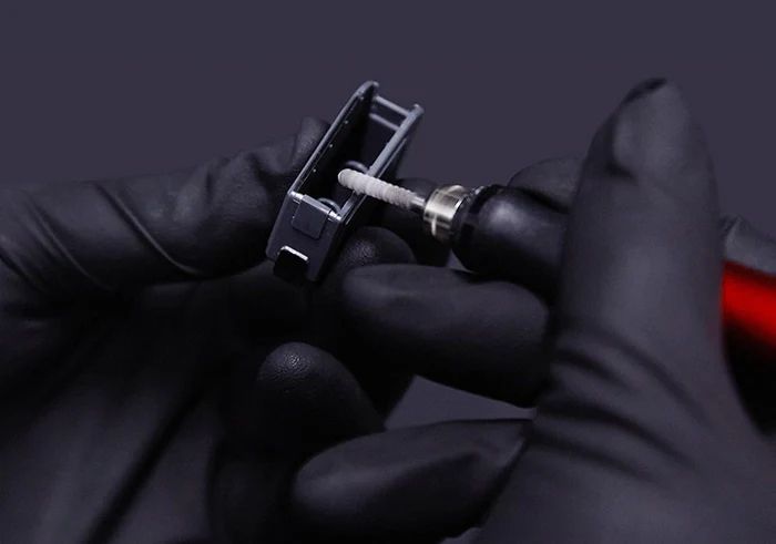 A gloved hand smoothing a grey plastic part with the DSPIAE ES-P sanding pen