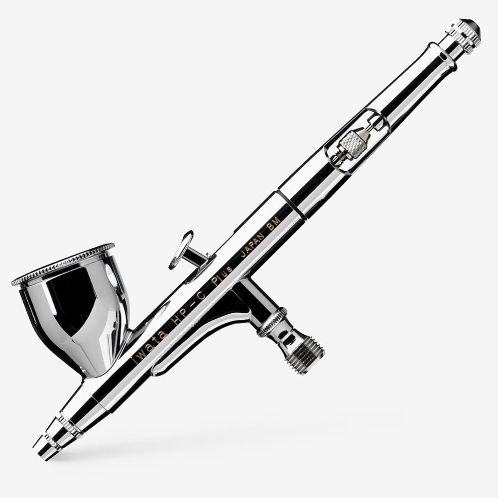 Iwata HP-C Plus airbrush on white, three-quarter view showing cup, trigger and hose fitting
