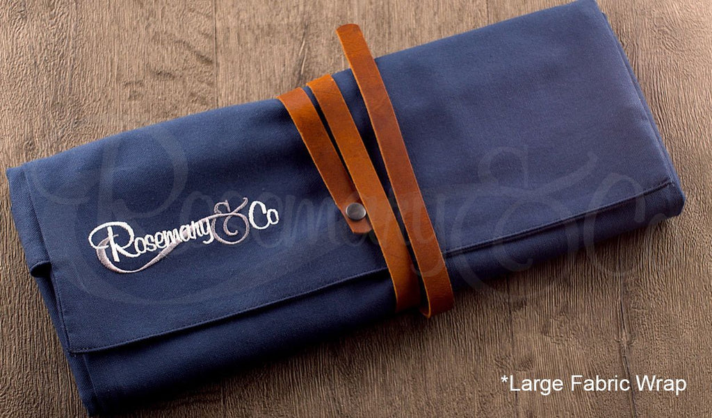 Rosemary & Co large fabric brush wrap shown closed on wooden surface with navy canvas body and leather strap