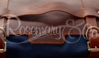 Close-up of Rosemary & Co leather fabric brush wrap showing engraved logo, leather carry handle, buckle straps and navy canvas body
