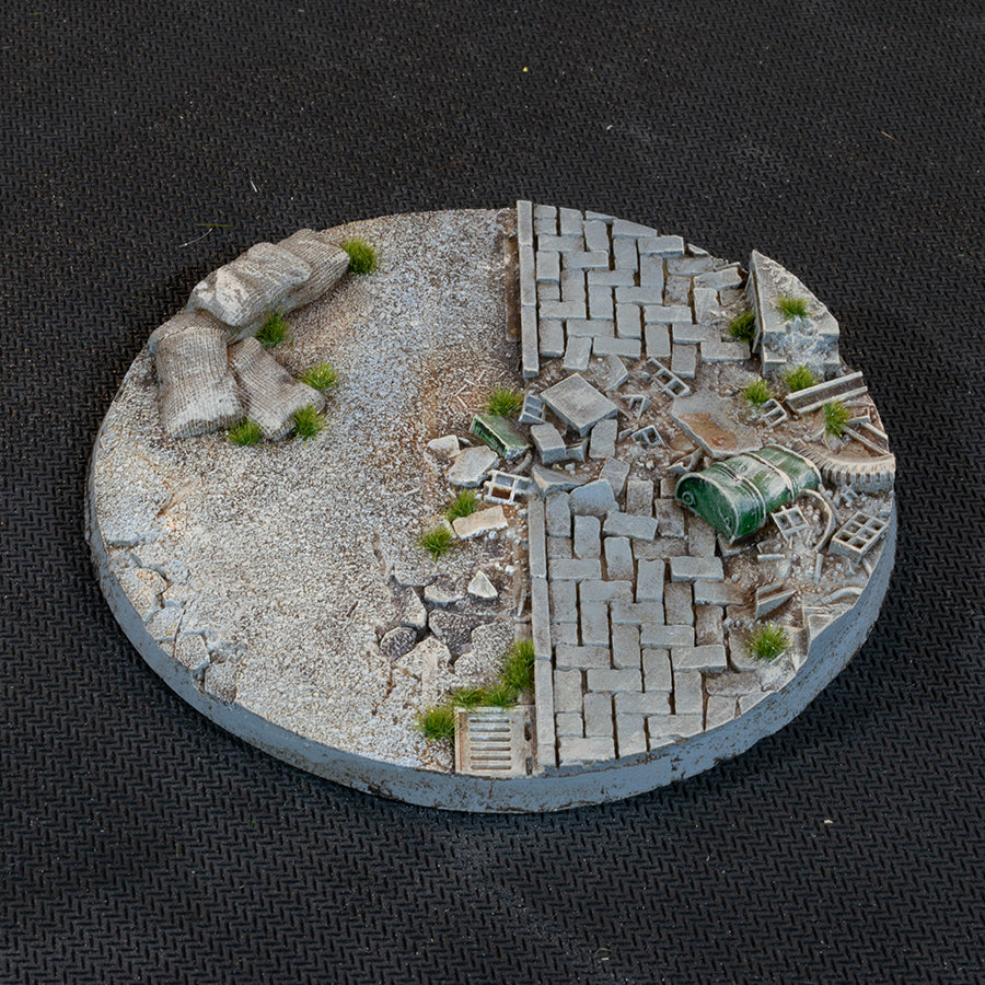The 100mm base seen from above: a band of gravel dividing two stretches of paving, drum and crate among the debris