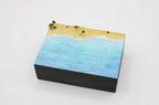 A finished shoreline diorama painted on a water sheet: turquoise sea and white surf meeting a sand beach